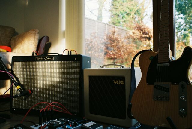 A Telecaster guitar, two amplifiers, and a selection of pedals in a sunlit room. One of the amplifiers has a microphone positioned in front of it.