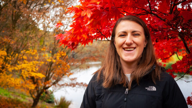 Annika stood under a vibrant red autumnal tree by Winkworth Arboretum lake in Godalming.